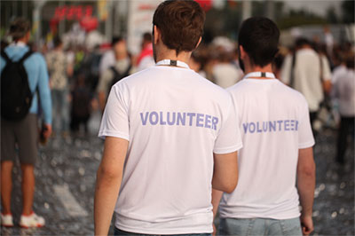 2 young men, photographed from behind,  wearing "volunteer" tshirts