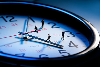 Tiny professionals walking along the face of a giant timeclock