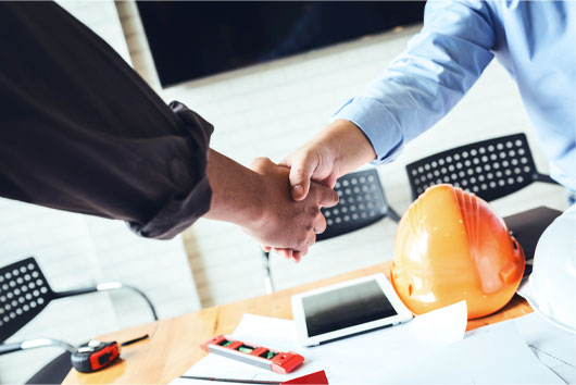 close up of handshake between 2 men; hard hat in background