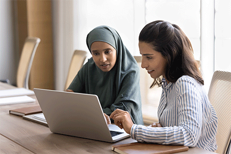 Two focused young Arab and Hispanic managers women working at laptop together, 