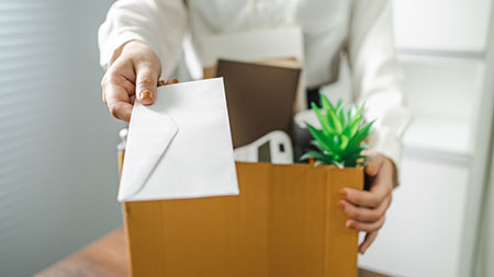 close up of woman holding box with personal items from office desk handing over envelope with resignation notice