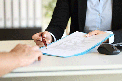 close up, hands of  2 people across table from each other, one handing paperwork and pen to other