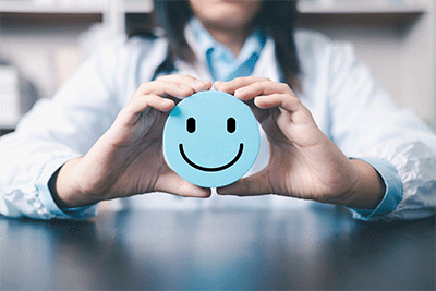 close up showing hands holding blue happy face; woman seated at table