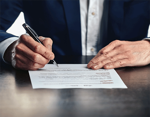 close up cropped photo showing man's hands holding pen, signing document on desk