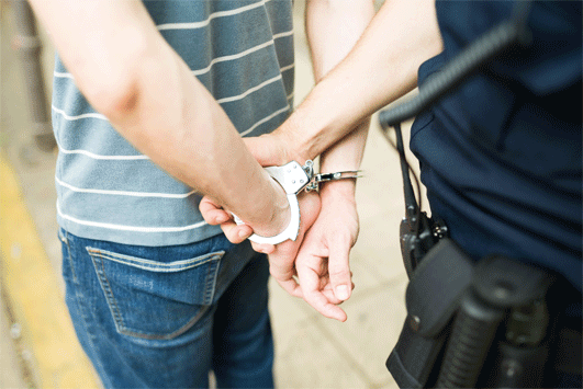 close up showing man with hands in handcuffs behind his back and officer holding his wrists