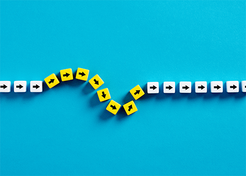 plastic cubes with arrows in straight line interrupted by series of yellow cubes with arrows that create a curve in the lineagainst blue background